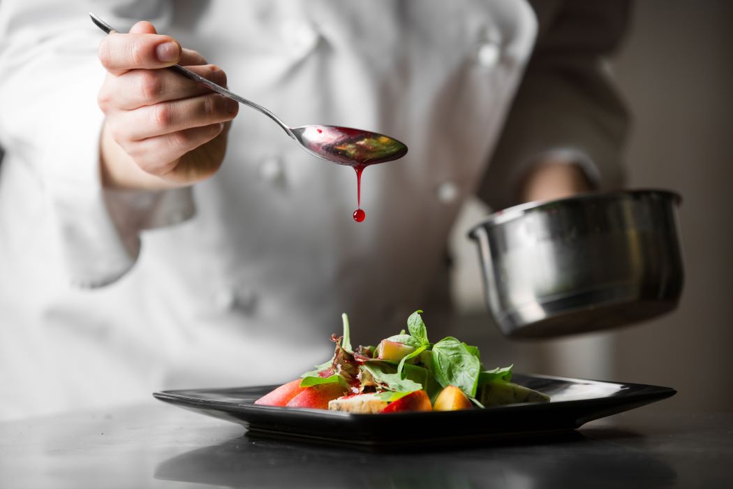 Xef amanint una amanida gourmet en un plat negre amb una cullera, mentre aboca una salsa vermella durant l’emplatat.