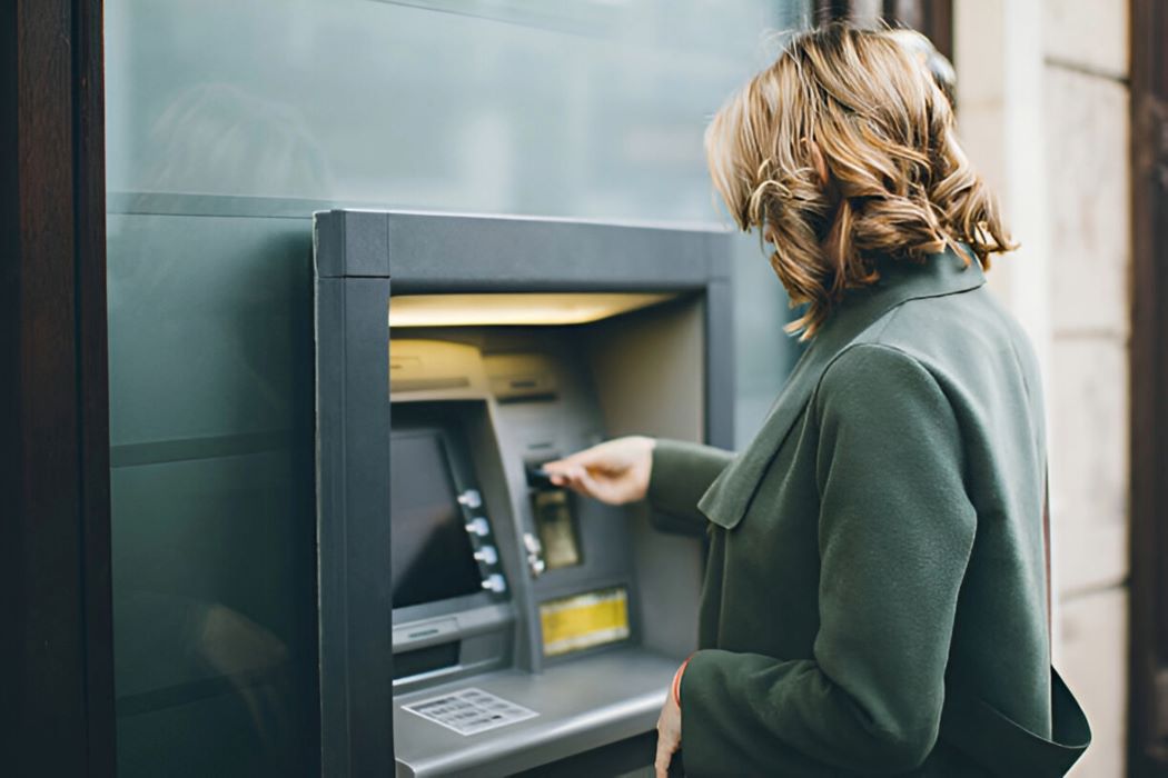Una dona d'esquena introdueix una targeta en un caixer automàtic