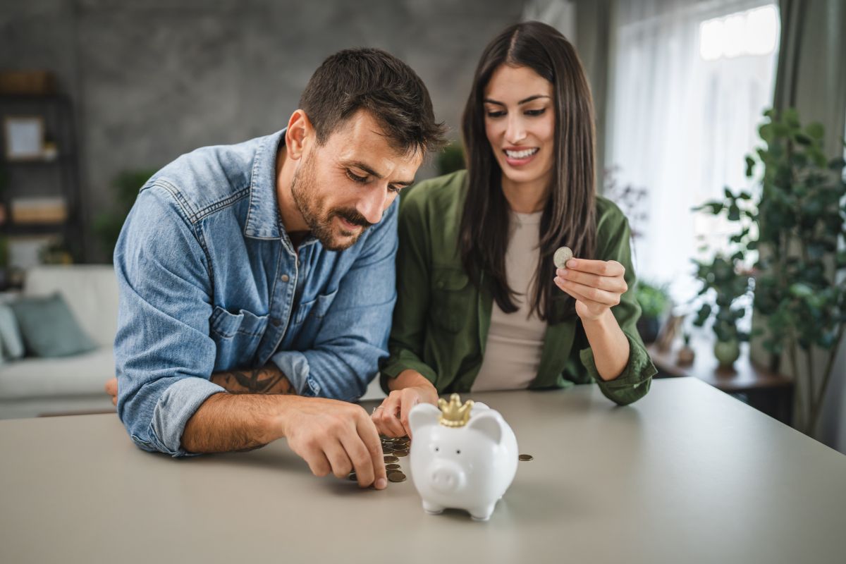 Personas contando monedas junto a una hucha sobre una mesa en el hogar, representando el ahorro, la planificación financiera y la gestión del dinero