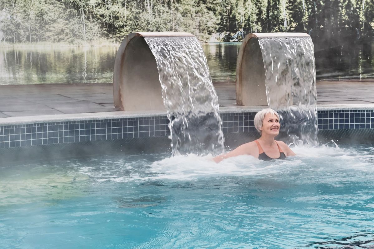 Persona gaudint d’un circuit d’aigües en una piscina termal amb cascades d’hidromassatge en un entorn de benestar.