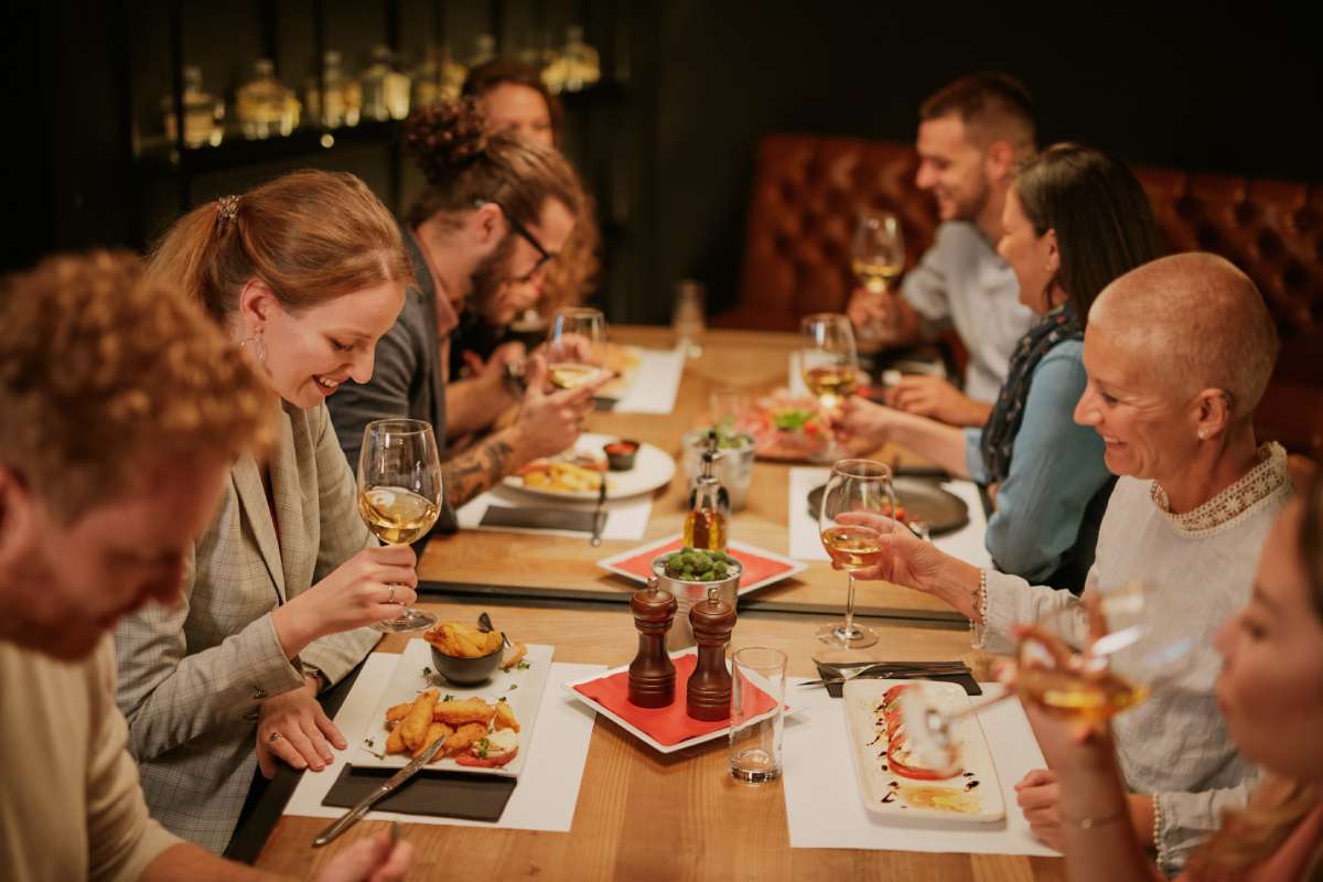 Grupo de personas compartiendo una comida en un restaurante, sentadas alrededor de una mesa con platos y copas, en un ambiente cálido e iluminado.