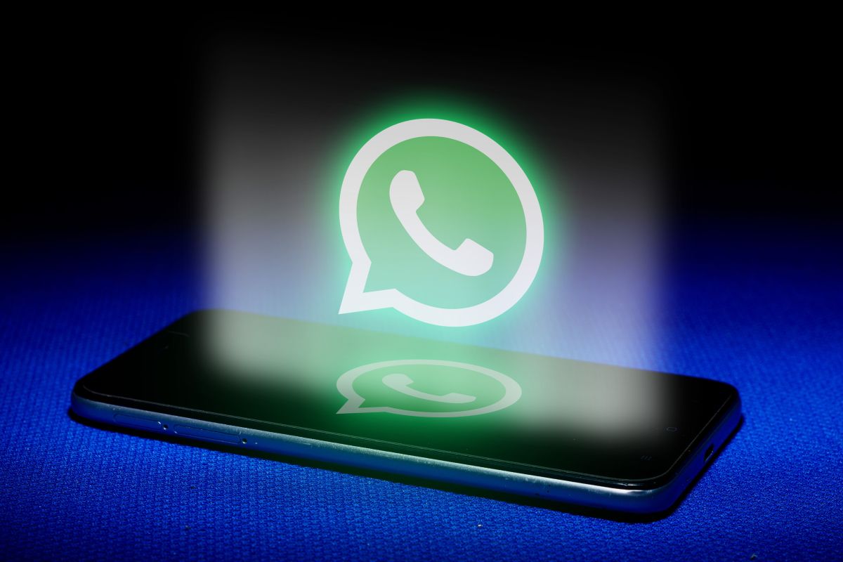 Teléfono móvil sobre una superficie azul con el logotipo de WhatsApp iluminado en verde sobre la pantalla