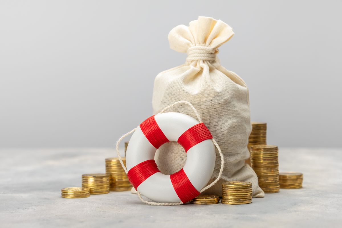 Saco de tela rodeado de pilas de monedas y un salvavidas blanco y rojo en primer plano.