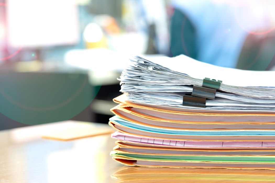 Pila de documentos y carpetas archivadas sobre una mesa, sujetas con una pinza, en un entorno de oficina