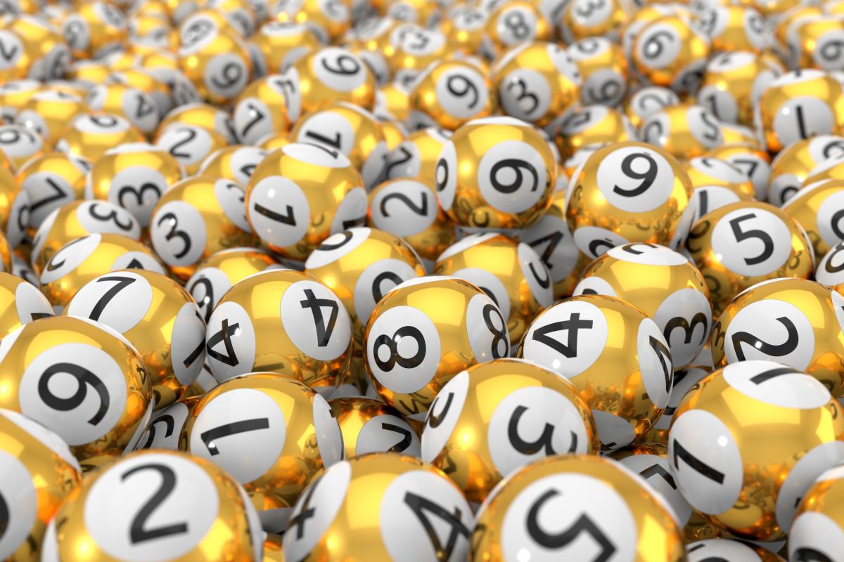 Numerosas bolas doradas con círculos blancos y números negros, amontonadas y distribuidas de forma aleatoria, evocando un sorteo de lotería.
