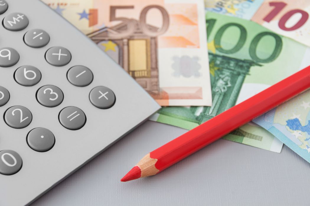 Calculadora, billetes de euro y un lápiz sobre una superficie, relacionados con la revisión de una declaración de la renta
