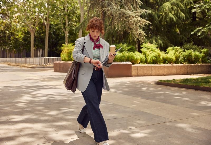 Una mujer joven pasea por un parque mirando su reloj