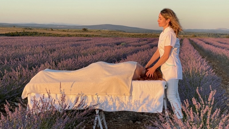 Una mujer da un masaje a una paciente tumbada en una camilla en un campo de lavanda