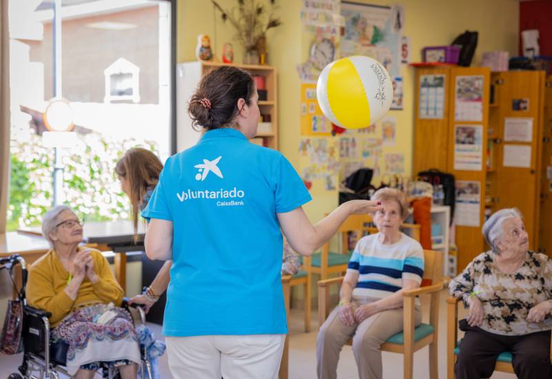 Una voluntaria de CaixaBank juega, rodeada de mayores, con una pelota hinchable