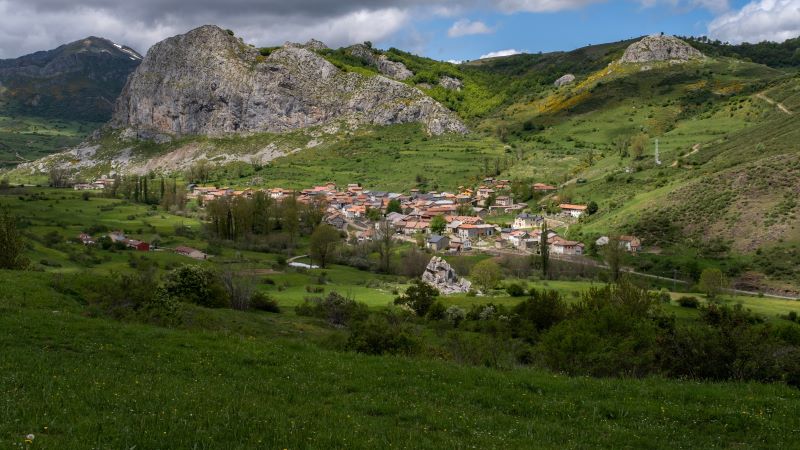 Maraña: pueblo de montaña en la Cordillera Cantábrica Pueblo de montaña en valle verde con casas de teja roja, rodeado de praderas y formaciones rocosas, bajo cielo parcialmente nublado