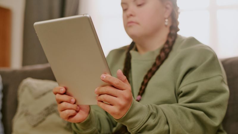 Mujer joven con trenzas usando una tablet en el sof&aacute; de casa, en primer plano, con iluminaci&oacute;n c&aacute;lida y fondo desenfocado