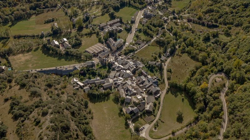 Ribera de Cardós (Lleida): la belleza del Pirineo Vista aérea de Ribera de Cardós, con casas agrupadas en el centro, carreteras sinuosas, campos y bosques alrededor en un paisaje rural de montaña