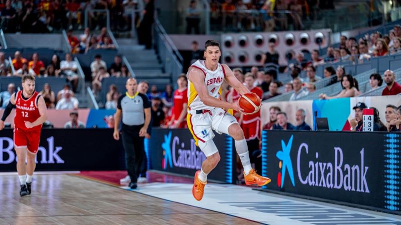 Deportista de la selecci&oacute;n espa&ntilde;ola de baloncesto salta con el bal&oacute;n en partido, con p&uacute;blico en gradas y publicidad de CaixaBank junto a la pista