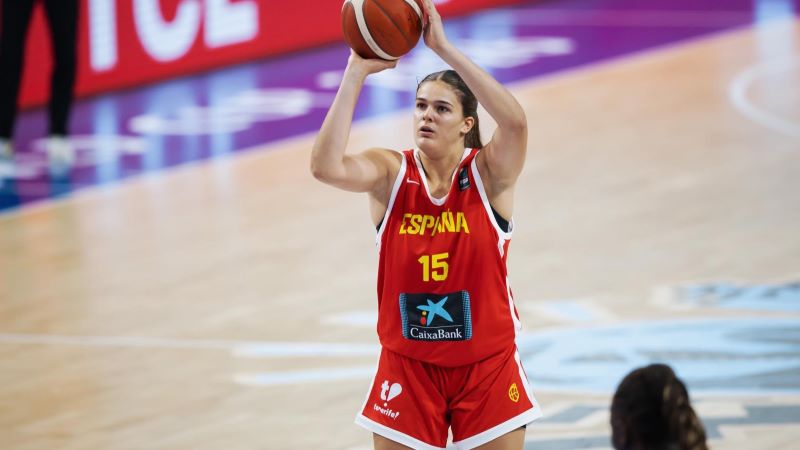 La equipación femenina de baloncesto está confeccionada con prendas elásticas, pero no ceñidas al cuerpo, de elastano, poliéster y poliamida Jugadora de la selección española de baloncesto ejecutando un tiro libre en una pista de juego, con la equipación roja oficial y el balón sobre la cabeza