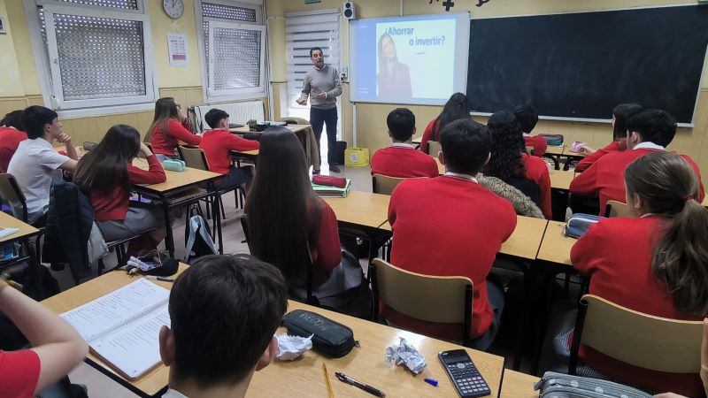 Adolfo, antiguo ingeniero de Caminos, explica a los jóvenes claves para el ahorro y el consumo responsable Un voluntario imparte una sesión de educación financiera en un aula, con alumnado sentado escuchando una presentación proyectada sobre ahorro e inversión