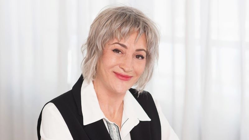 Elisabet Díaz, emprendedora y propietaria de TERRAHUT Retrato de estudio de Elisabet Díaz, con cabello corto y claro, vestida con camisa blanca y chaleco oscuro, sentada frente a una cortina blanca.