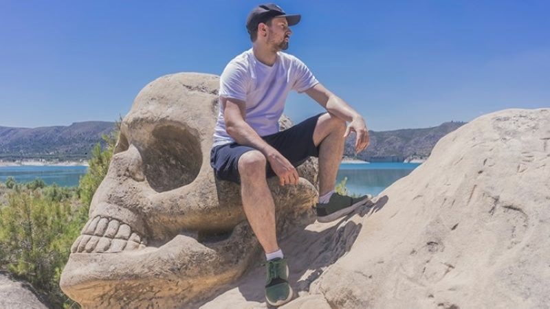 un joven turista se apoya en una calavera tallada en piedra dentro de la ruta de las Caras de Buend&iacute;a, en Cuenca